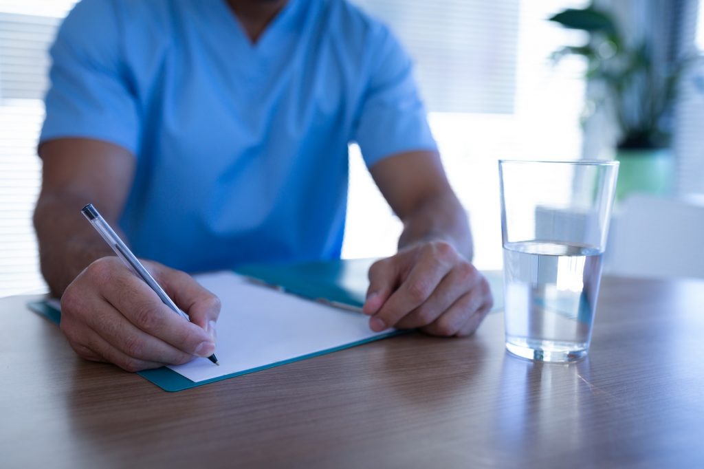 Mid section of Caucasian male surgeon writing on medical chart in clinic at hospital